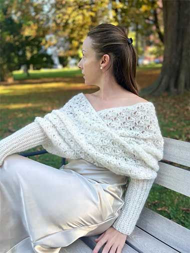 Light gray crochet sweater scarf with textured stitches and long sleeves worn on a park bench in autumn.