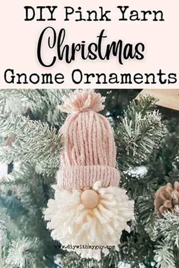 Pink yarn Christmas free DIY gnome ornament with a fluffy beard and hat, hanging on a snowy tree branch.