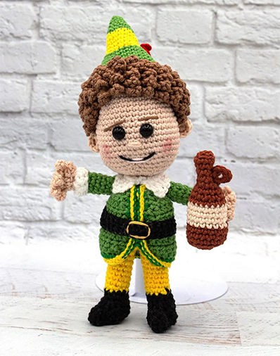 Crochet Buddy the Elf amigurumi holding a bottle, crafted using an elf amigurumi crochet pattern for holiday fun.