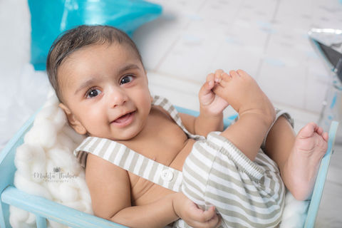 Smiling baby boy in striped overalls, posing on a wooden crate. baby photographer in mumbai