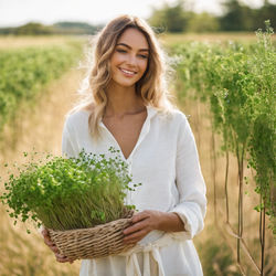 beautiful woman wearing white standing outside in a linen clothes line holding microgreens