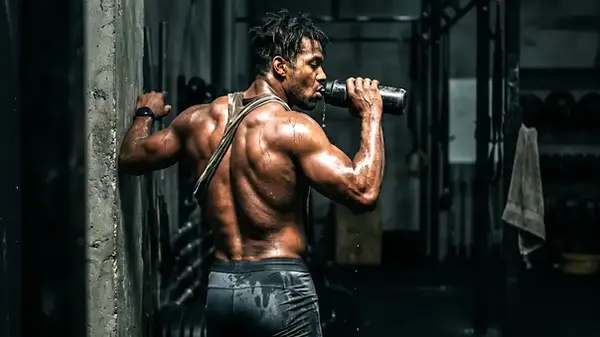 Homem musculoso suado bebendo em garrafa após treino