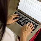 Mãos digitando em um laptop com texto na tela.