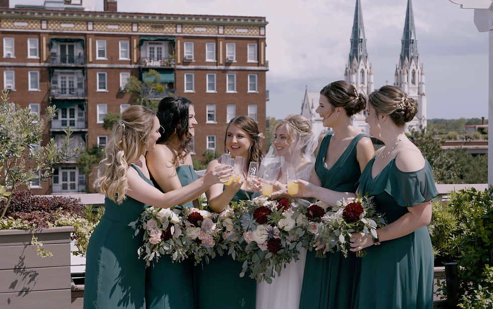 Wedding photography and videography example of a group of bridesmaids posing on top of a rooftop in Savannah, Ga with the famous cathedral in the background.