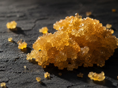 Gros plan d'un fragment de crumble CBD doré sur ardoise sombre, texture granuleuse et reflets cristallins
