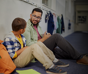 Image of student and teacher sitting on the floor talking. Showing that this teacher is helping the student in a time of need.