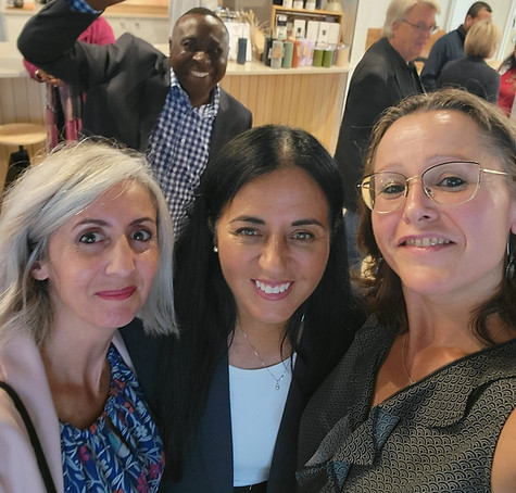 Trois femmes souriantes en selfie, homme en arrière-plan