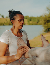 Femme masseuse pratiquant la réflexologie plantaire en plein air près d'un lac.