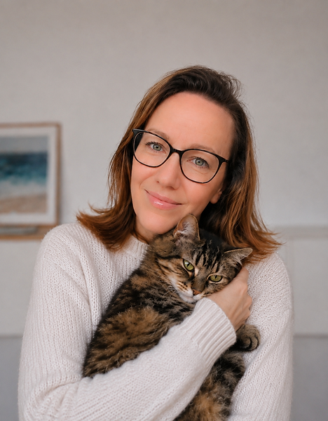 Femme souriante à lunettes serrant un chat tigré.