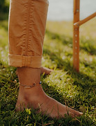 Bas de jambe avec pantalon marron, pied nu sur l'herbe verte.