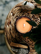 Bougie allumée, bâtonnets de palo santo, herbes séchées sur porte-bougie tressé.