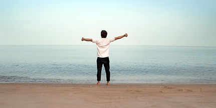 Homme sur une plage, bras ouverts face à la mer.