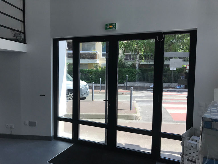 Portes vitrées d'entrée avec panneau de sortie vert, vues sur rue et voiture.