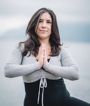 Femme en pose de yoga, mains jointes, près de l'eau.