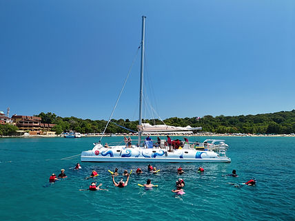 Group swimming in blue water beside a white catamaran.