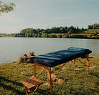 Table de massage au bord d'un lac ensoleillé sur l'herbe verte.
