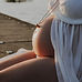Femme enceinte assise sur un quai, un collier sur le ventre