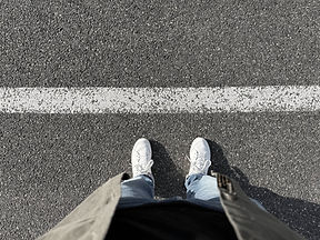 Deux pieds en baskets blanches devant une ligne épaisse sur l'asphalte.