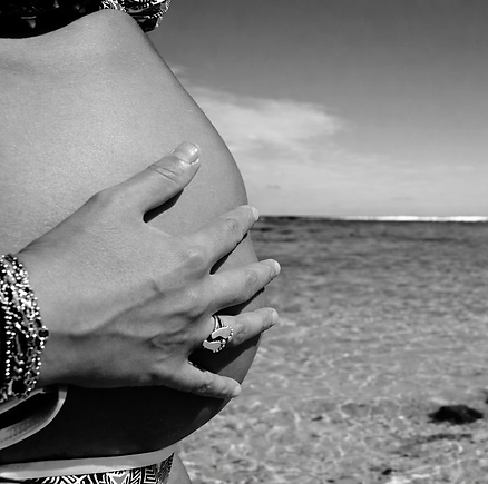 Main caressant ventre de femme enceinte, plage et océan en arrière-plan.
