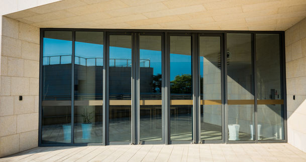Grandes portes vitrées modernes reflétant le ciel d'un bâtiment contemporain.