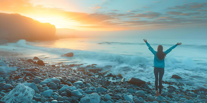 femme-sur-une-plage-rocheuse-au-lever-du-soleil-bras-leves-se-sentant-inspiree-par-la-natu