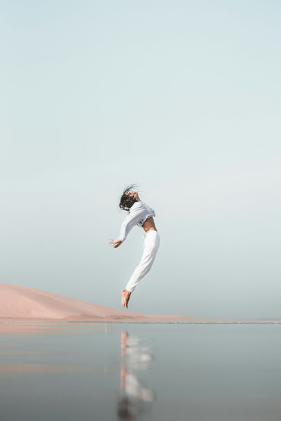 Femme sautant de joie sur une plage pour l'équilibre ayurvédique