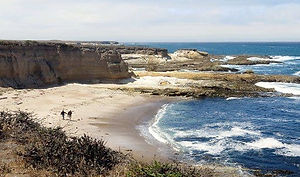 Personnes se promenant sur la plage ensoleillée avec l'océan et les falaises.