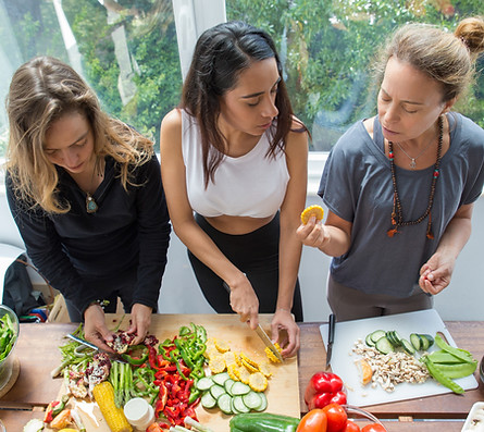 Trois femmes coupent des légumes frais colorés dans une cuisine lumineuse.