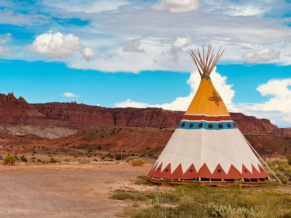 Tipi coloré devant le paysage désertique. Ciel bleu nuageux, montagnes en arrière-plan.