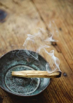 Palo Santo allumé fumant dans coupelle métallique sur table en bois.