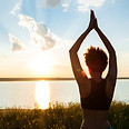 Femme pratiquant le yoga au coucher du soleil face à l'eau