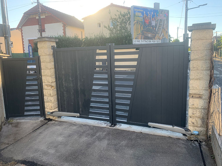 Portail automatique noir moderne avec motif géométrique et piliers en pierre.