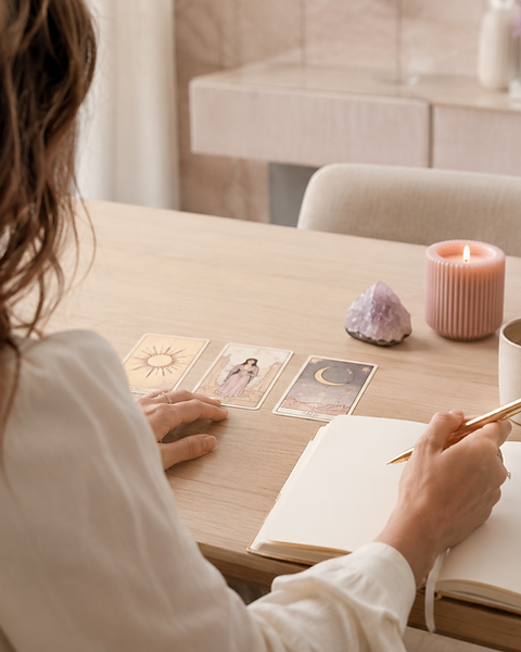 Femme écrivant dans un carnet avec cartes de tarot et bougie