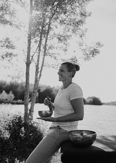 Femme souriante tient un bol, assise au bord d'un lac ensoleillé.