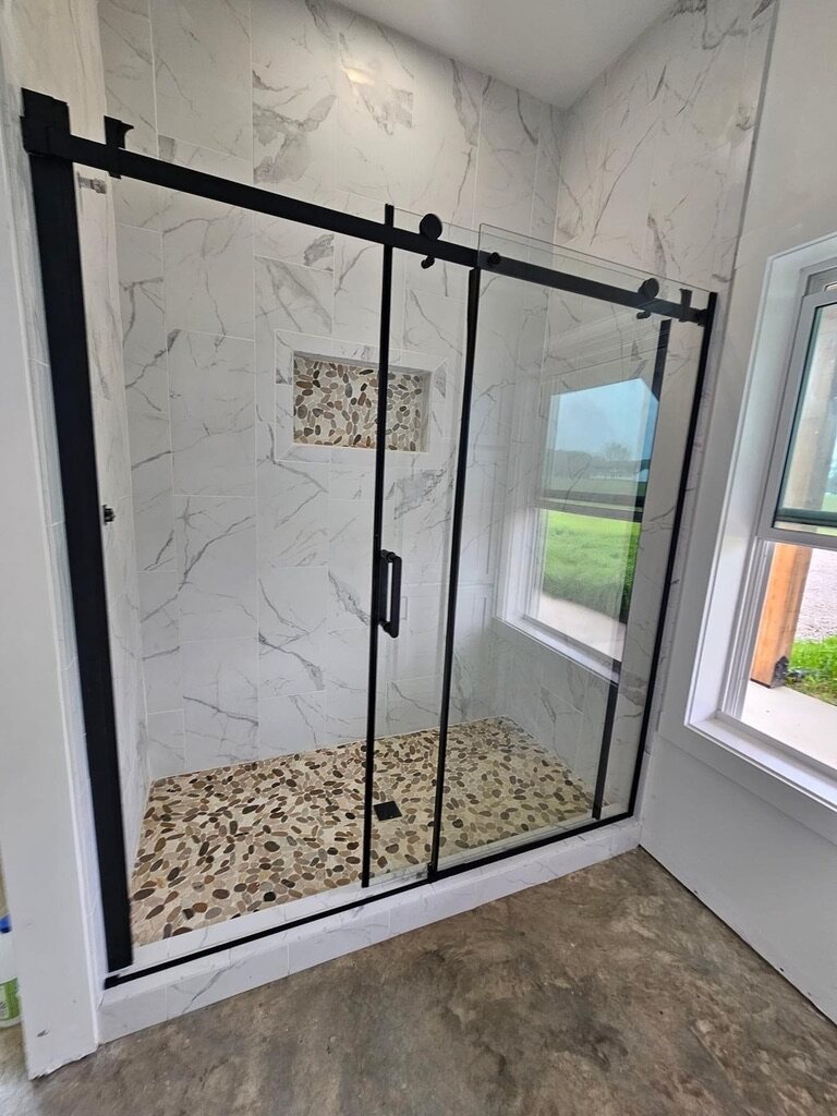 Frameless sliding-glass shower with a pebble floor and marble-look tile