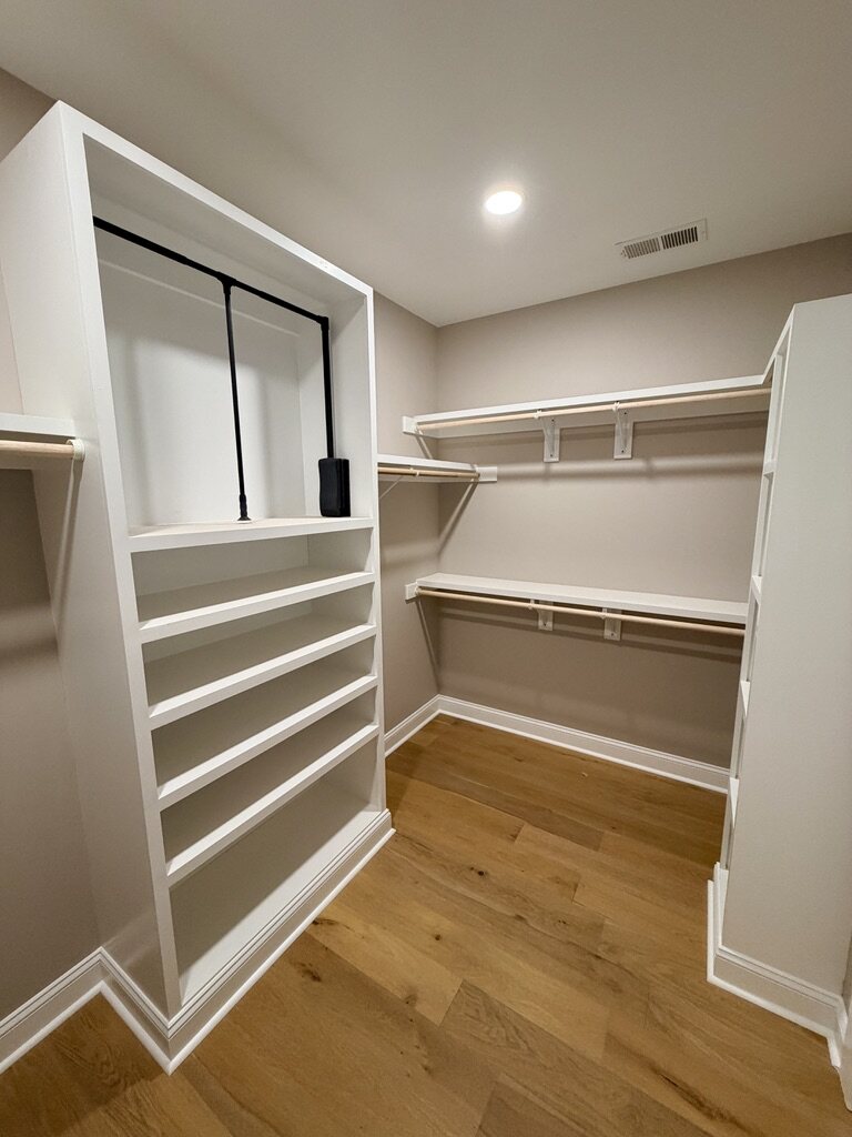 Walk-in closet with white built-in shelving and a pull-down rod
