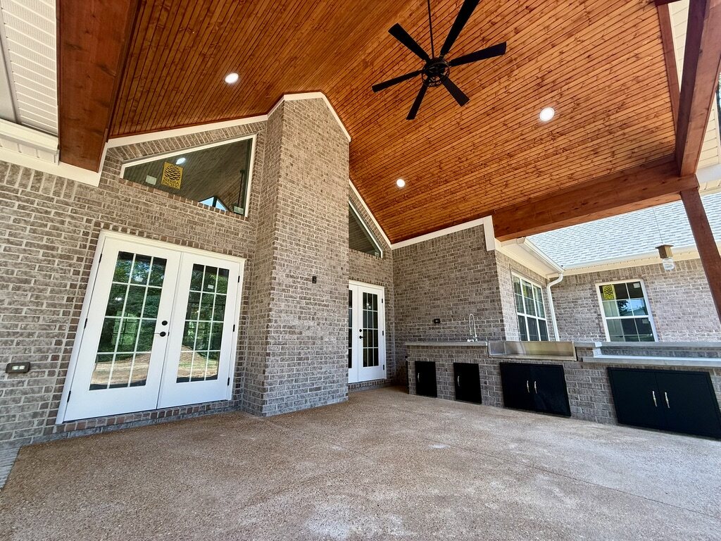Covered outdoor kitchen with a stained wood ceiling and brick walls
