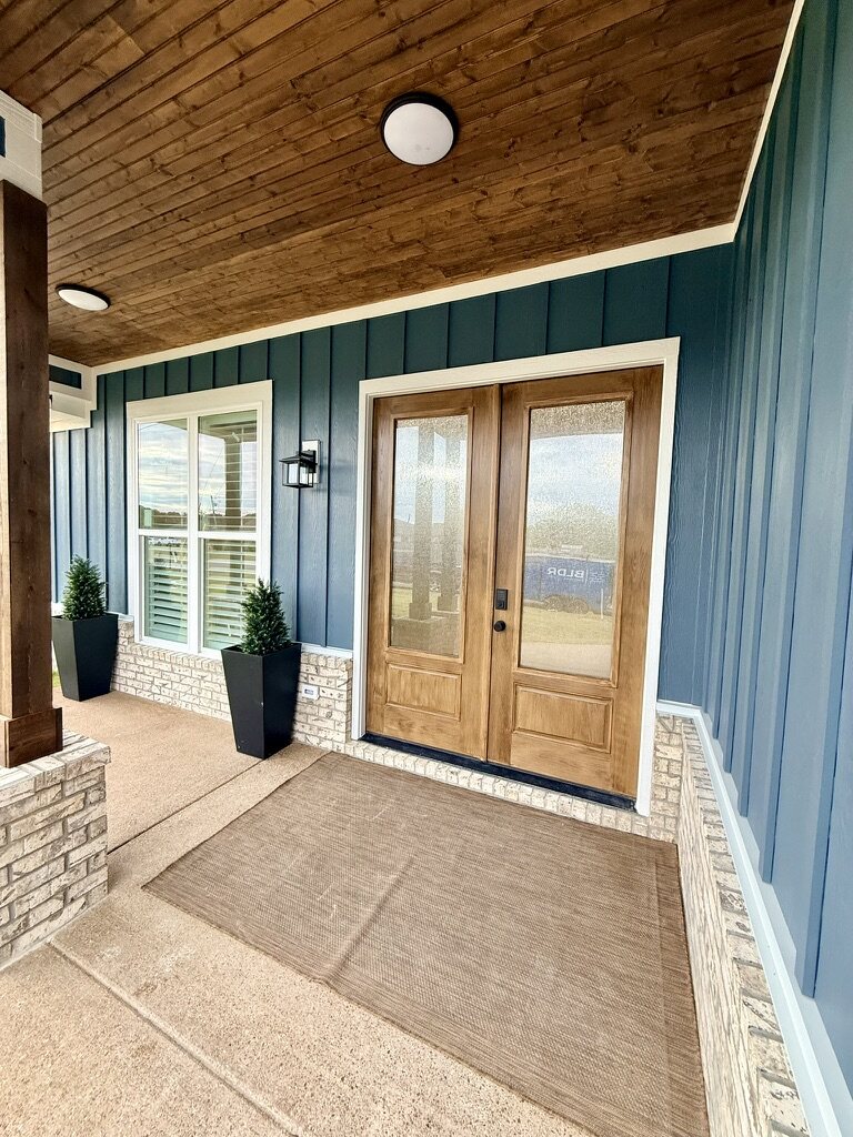Stained wood double front doors under a covered porch with a wood ceiling
