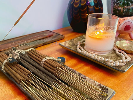 organic incense, a burning candle, soft orange glow, some white wooden prayer beads draped around a rustic display plate