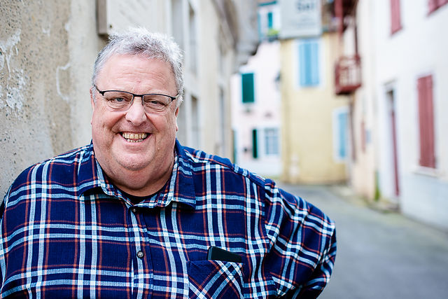 Personal branding photography for male entrepreneur shows him in cobbled French street smiling at camera in a head a shoulders shot for a lifestyle headshot photo