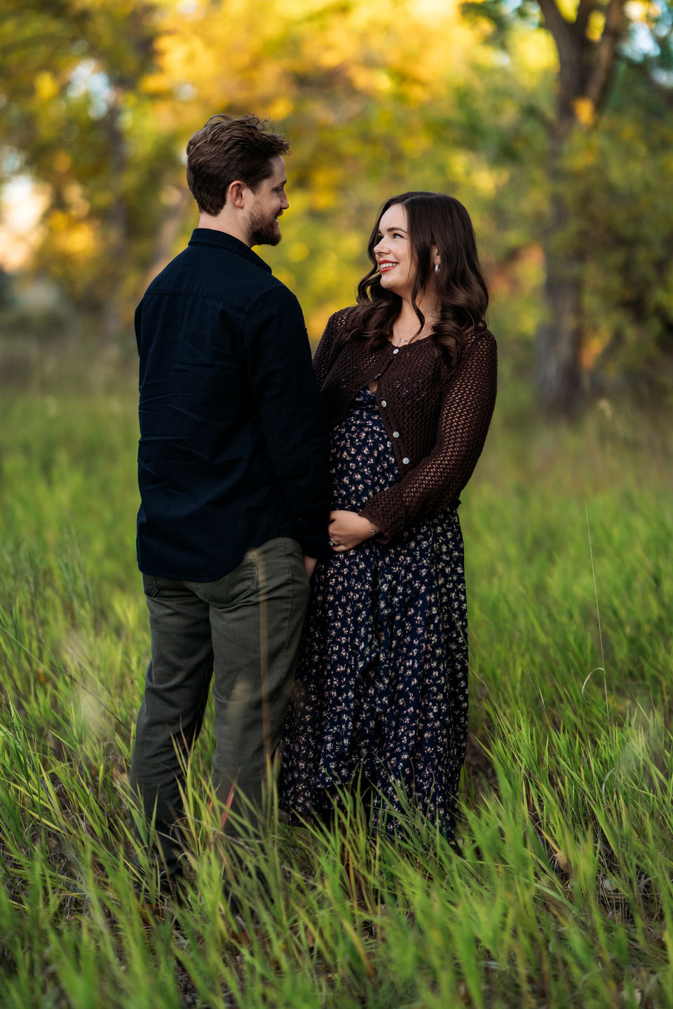 Pregnant mother smiling and cradling her belly outdoors in Fort Collins, Colorado, captured in a professional maternity photography session.