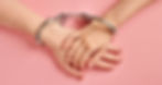 Two hands handcuffed together on a pink background