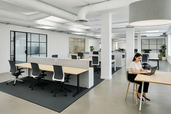 Open-plan office in Milton Keynes with bench desks, black framed glass partitions, and exposed ceiling ductwork.