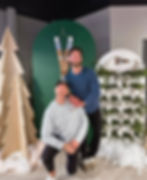 Two men posing at a winter-themed event with wooden trees.