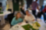 Two women smiling at a table during a past event.
