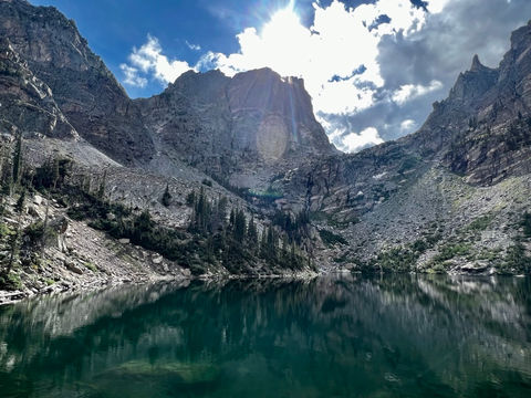 Ibón pirenaico en verano rodeado de montañas rocosas y reflejos en el agua
