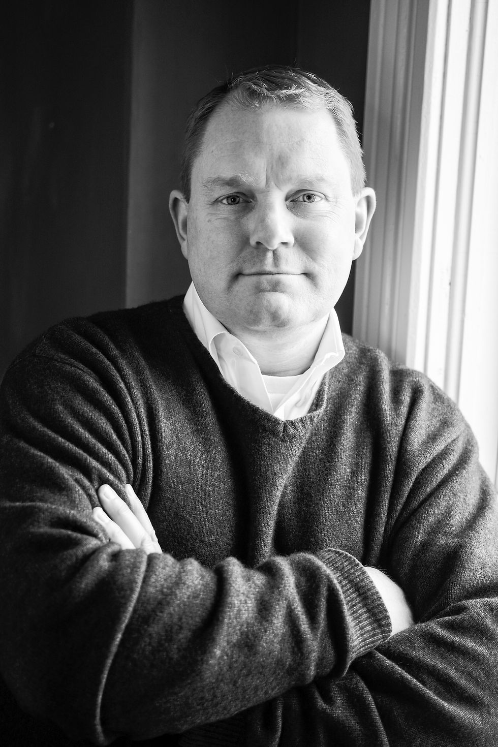 JR Olson standing next to a window with his arms crossed