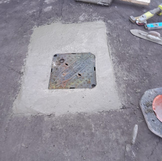 A fully repaired manhole and cover showing the cast iron square cover and surrounding concrete