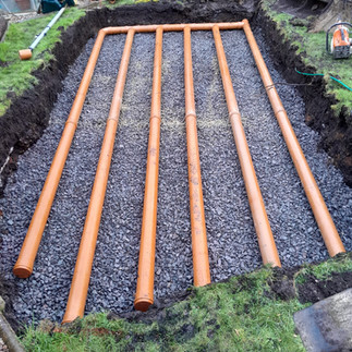 pipework for soakaway being laid over gravel - six long soakaway pipes in the excavated hole