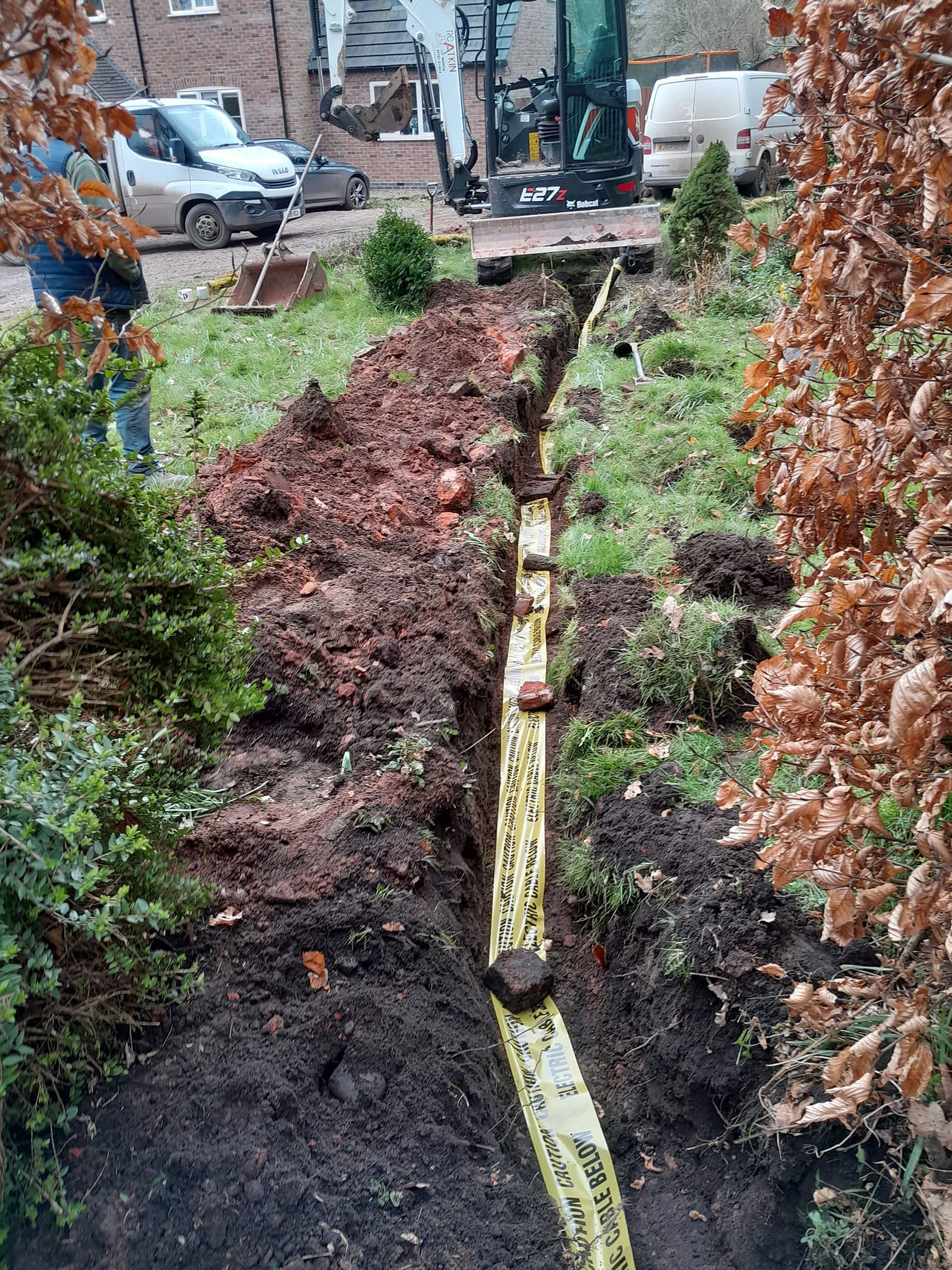 a long channel dug in a garden filled in with yellow exclusion tape laid on top to protect pipes underneath